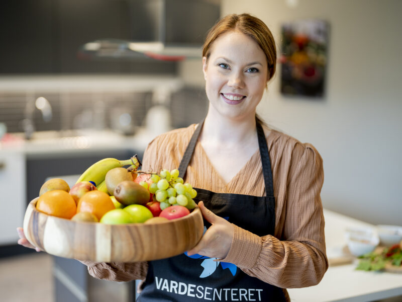 en kvinne i et forkle som holder en kurv med frukt.