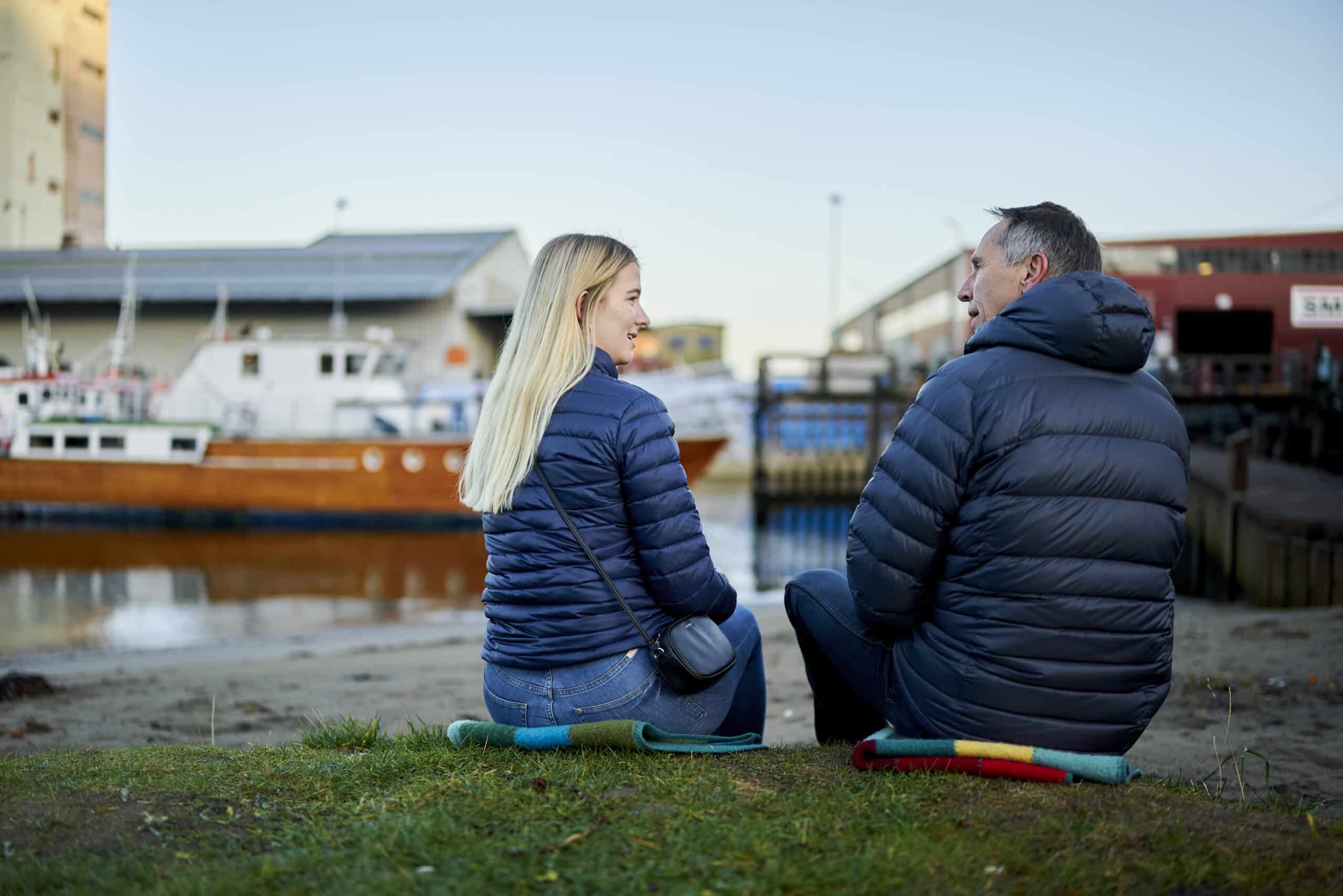 En mann og en kvinne sitter på bakken i nærheten av en båt.