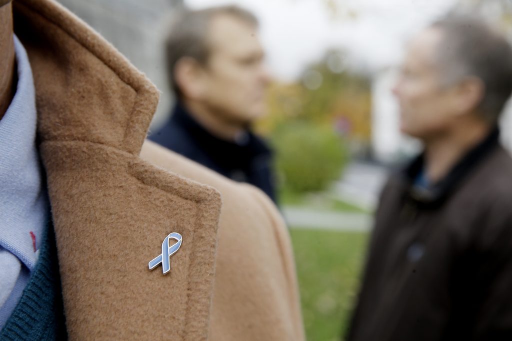 En Blå sløyfe-pin på en frakk, med to menn som snakker i bakgrunnen.