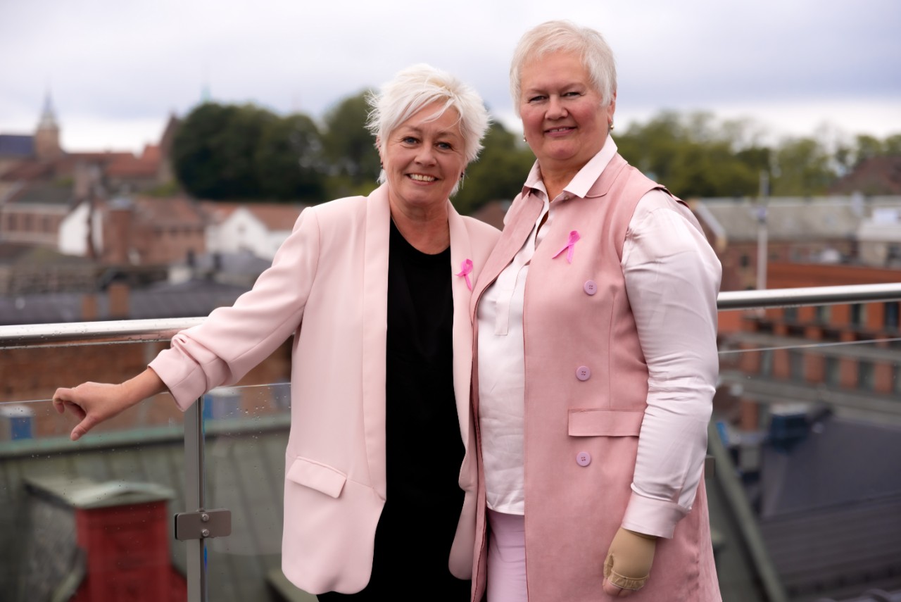 et par kvinner som står ved siden av hverandre ikledd rosa