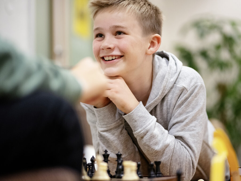 En smilende ung gutt spiller sjakk.