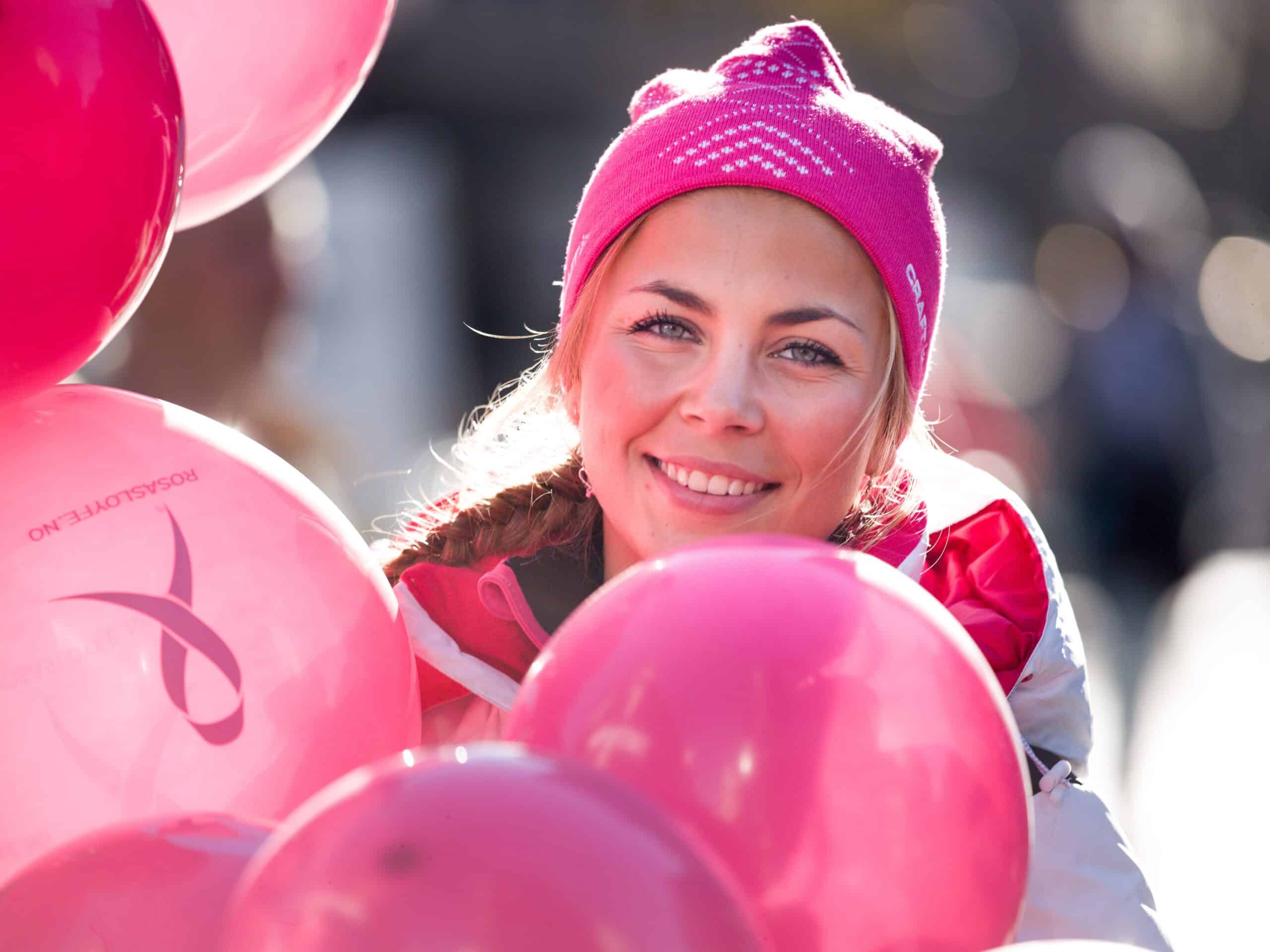 Smilende kvinne med Rosa sløyfe-ballonger foran seg.