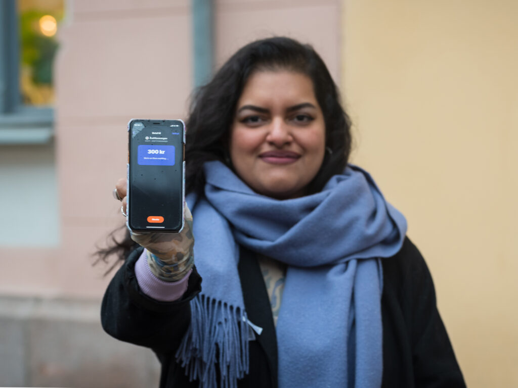 En kvinne holder opp mobilen og viser bilde av sendeskjermen i Vipps