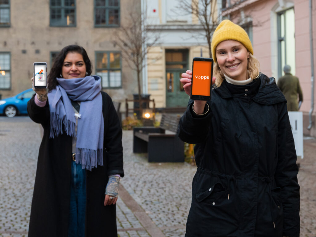To kvinner holder mobilene sine frem og viser bilder av en bøsse og Vipps-logoen
