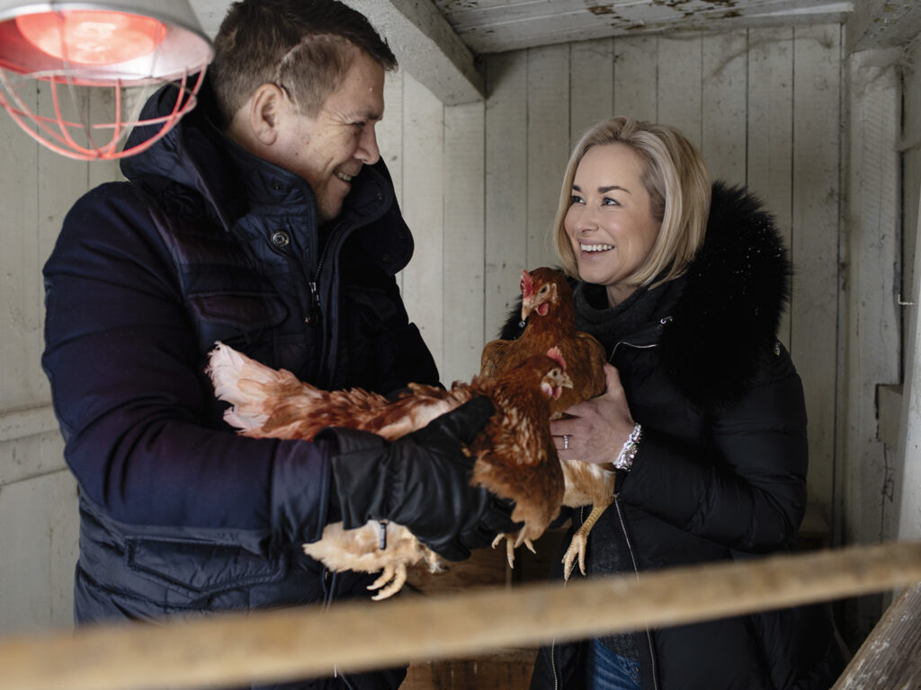 en mann og en kvinne holder høner i en låve.