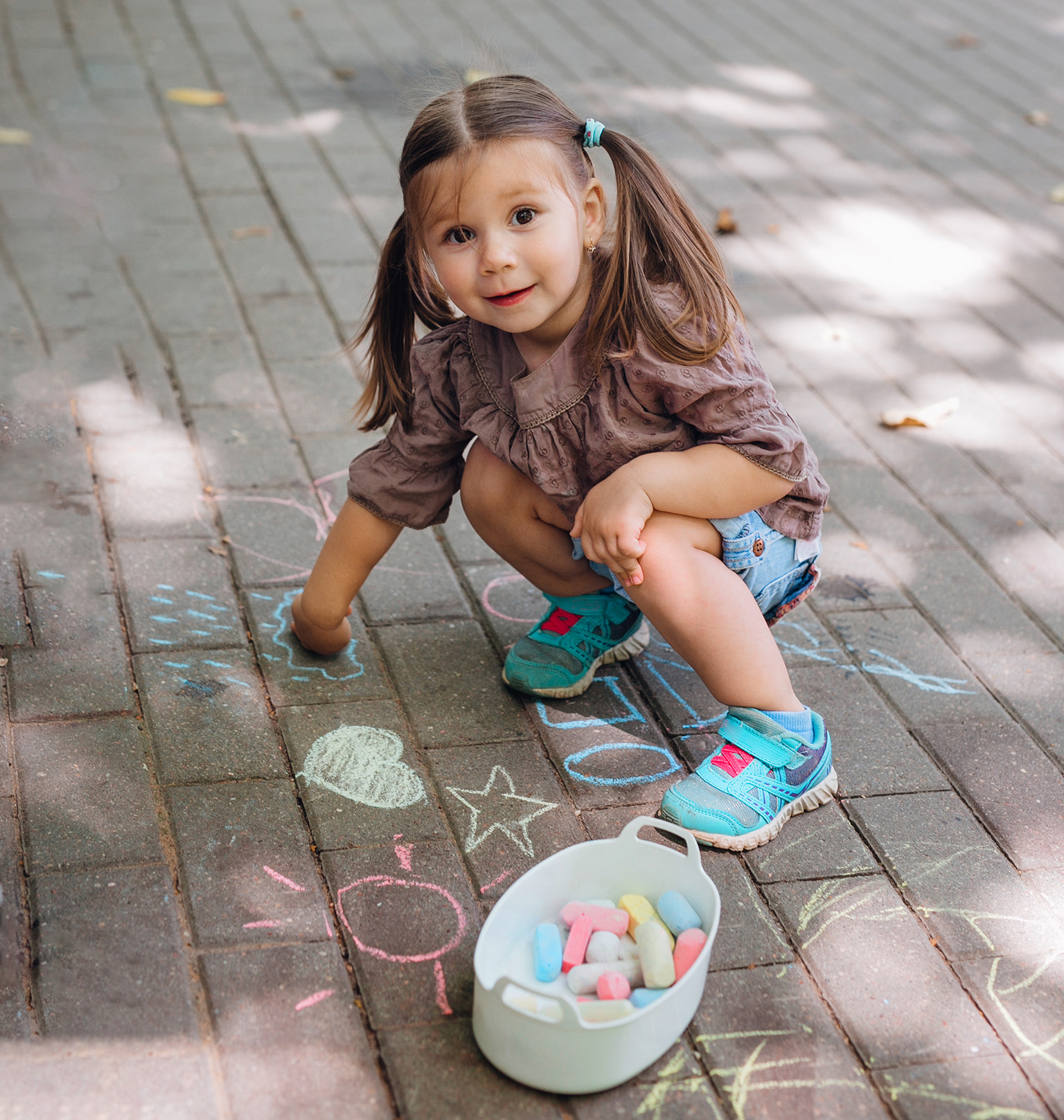 en liten jente som kneler ved siden av en bolle med kritt.