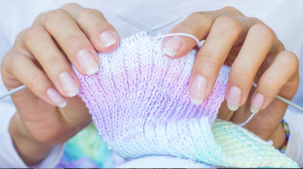 en kvinne som holder strikketøy i hendene.