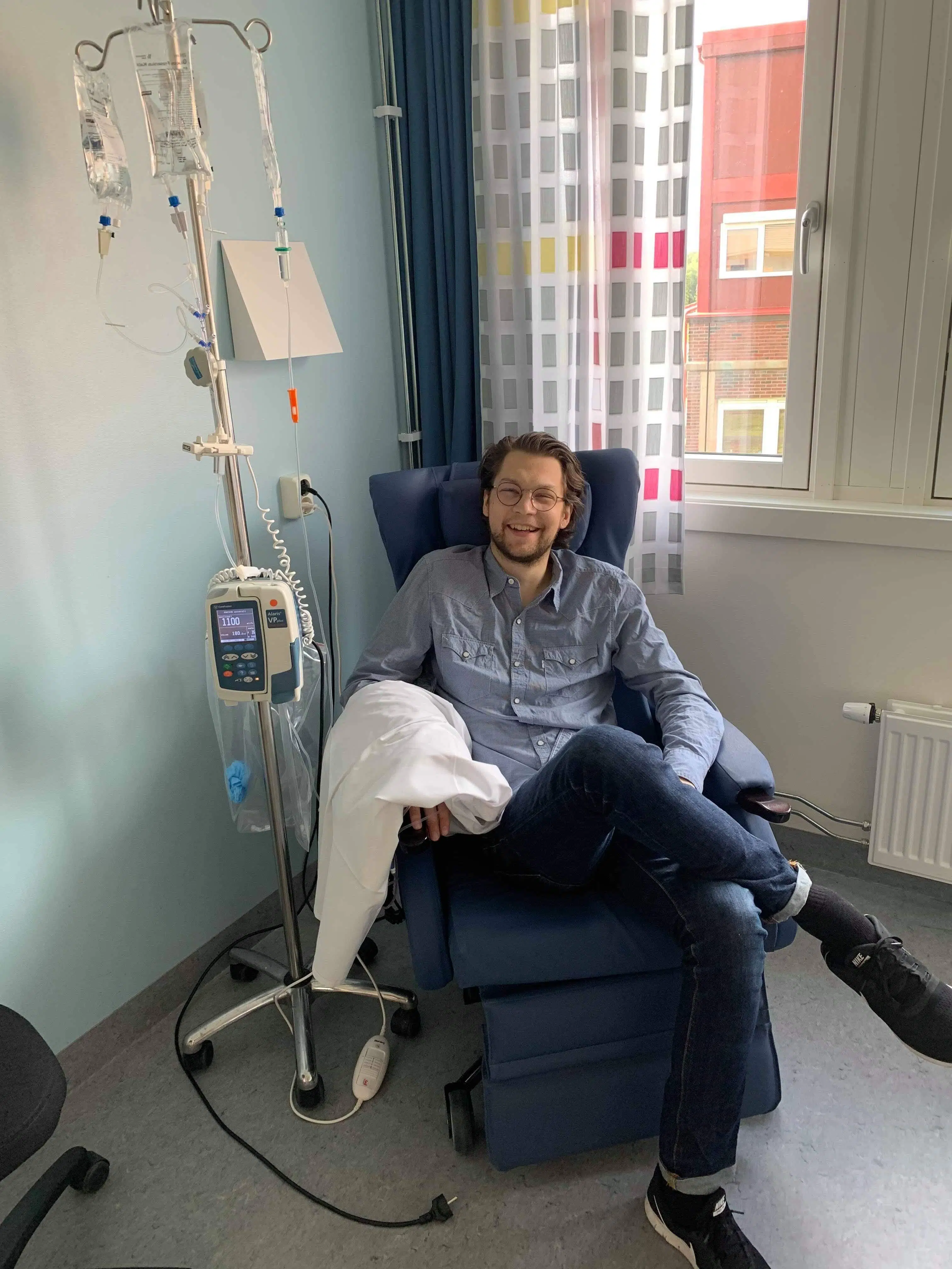 en mann som sitter i en stol på et sykehusrom.