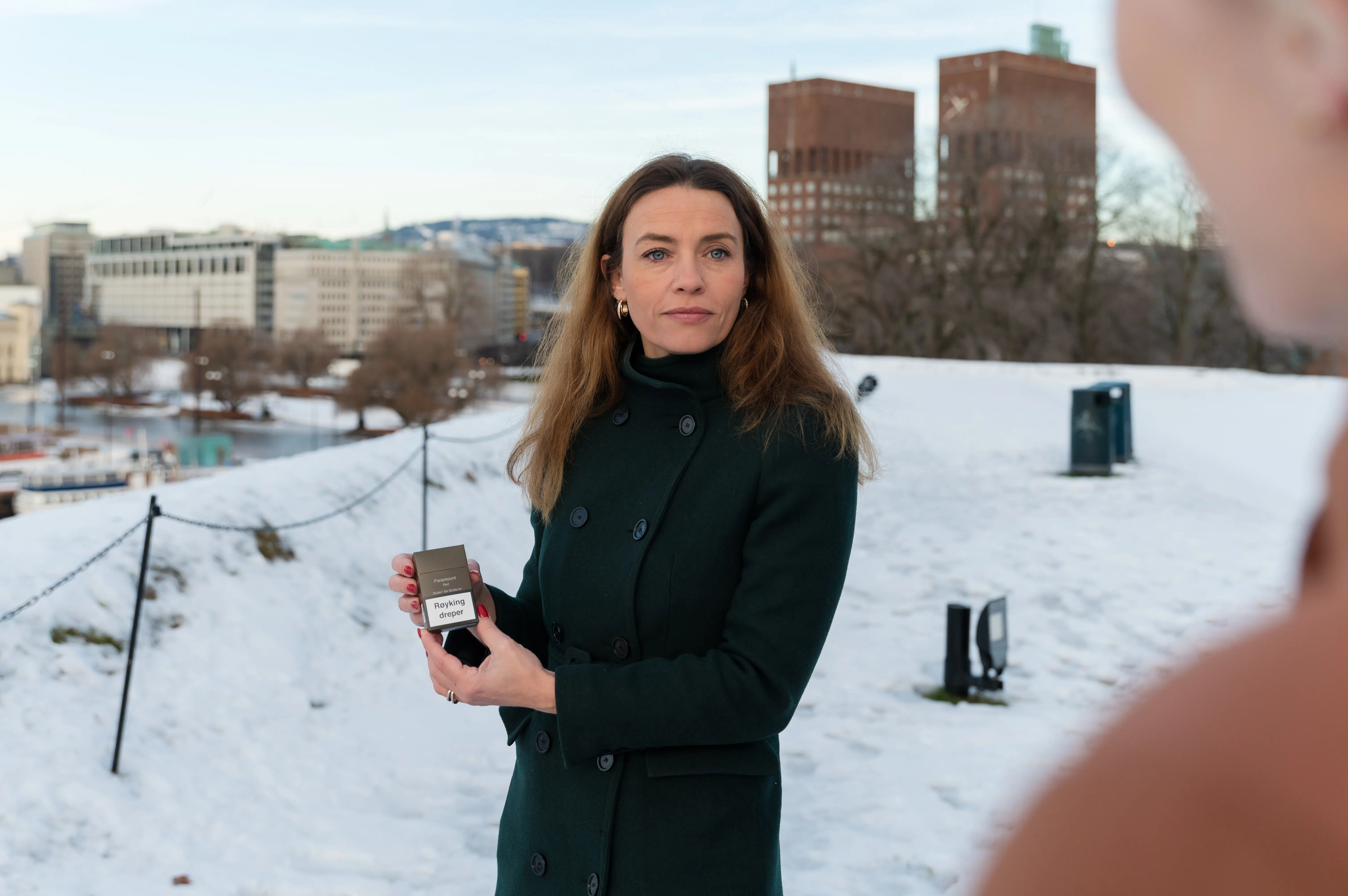 en kvinne som står i snøen og holder en sigaretteske.