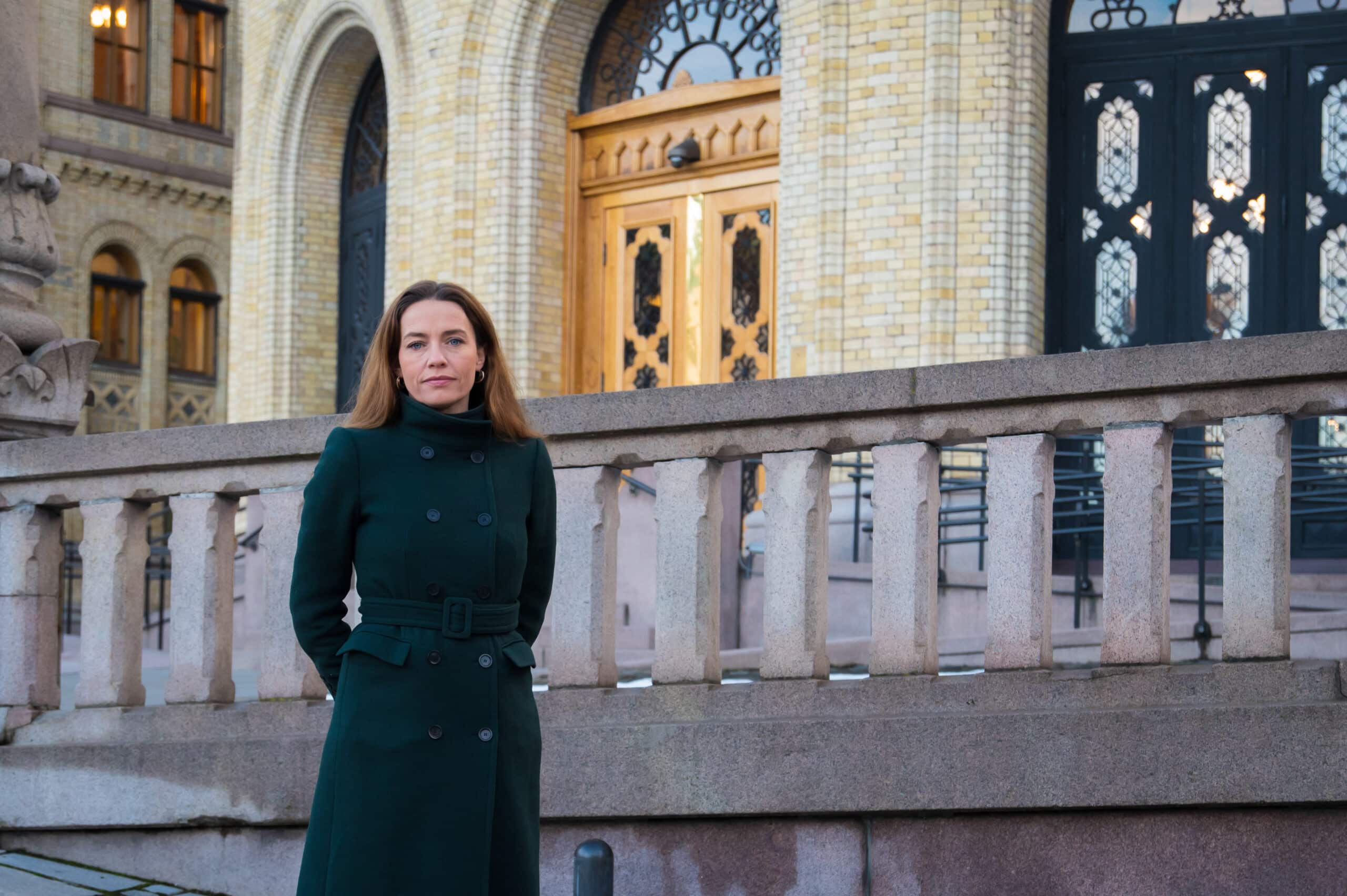en kvinne i grønn frakk som står foran en bygning.