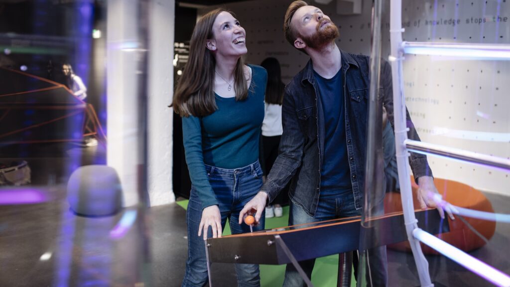 En mann og dame står og styrer en spak i et spill om DNA. Foto.
