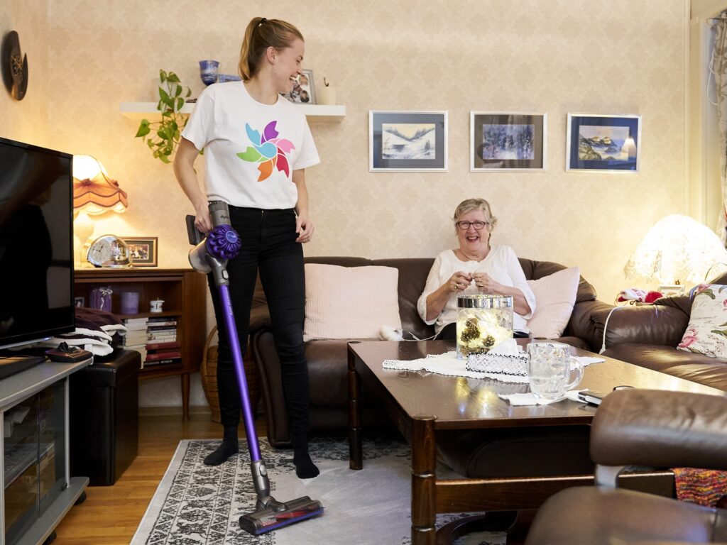 Ung kvinne hjelper eldre kvinne med støvsuging. Foto.
