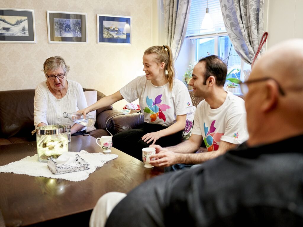 Yngre hjelpere drikke kaffe med eldre ektepar. Foto.