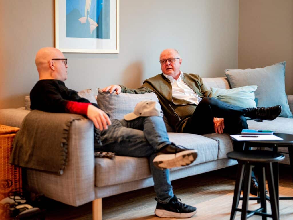 To menn som sitter i en sofa og snakker sammen.