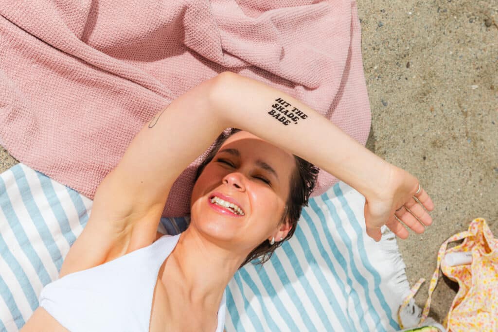 Kvinne med sol-tatovering på armen soler seg.