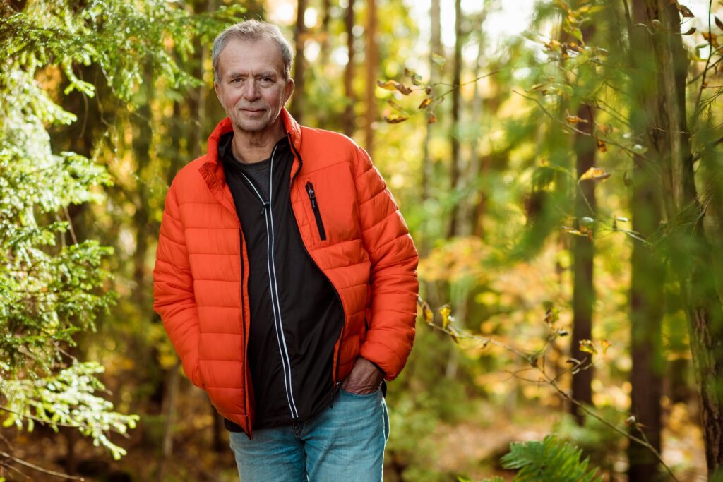 en mann i oransje jakke som står i skogen.