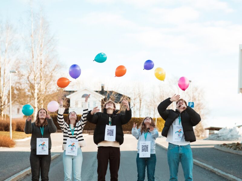 en gruppe mennesker som står på en gate og holder opp ballonger.