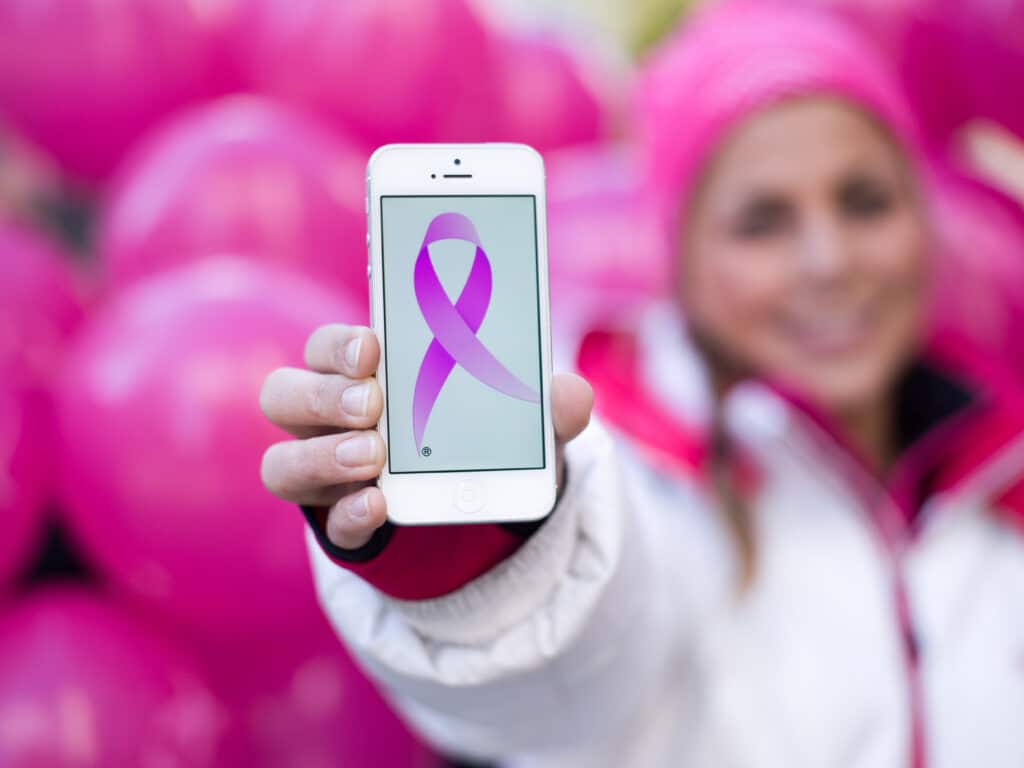 en kvinne som holder opp en mobiltelefon med et rosa bånd på.