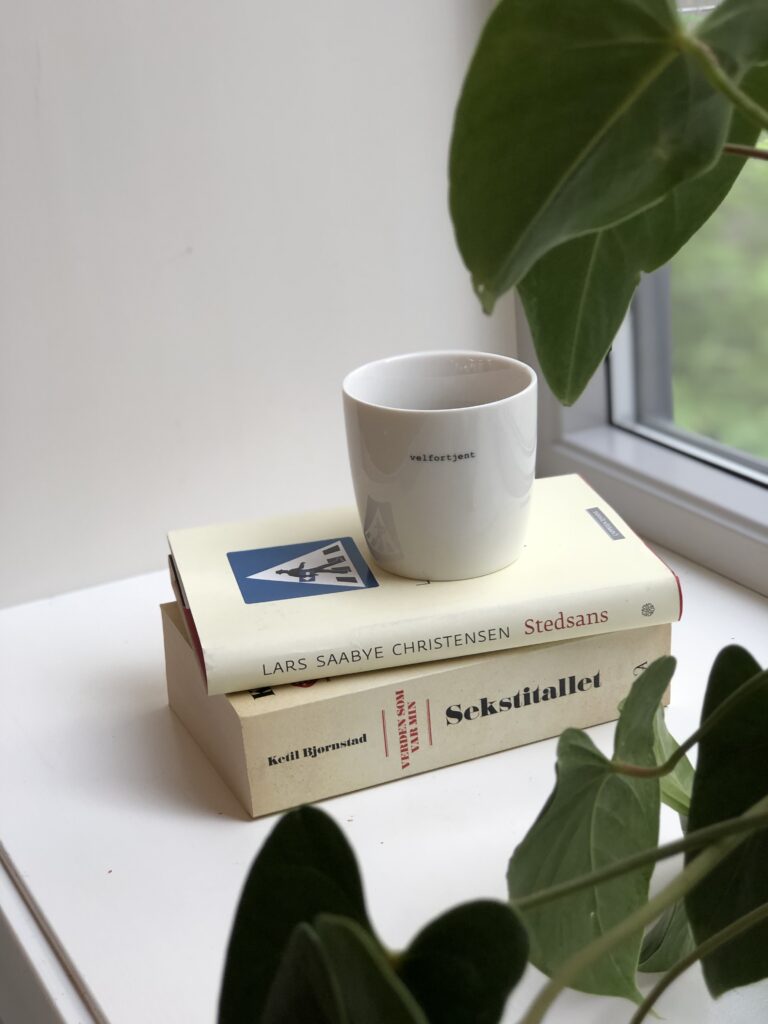 en kopp kaffe står ved siden av en bok i en vinduskarm.