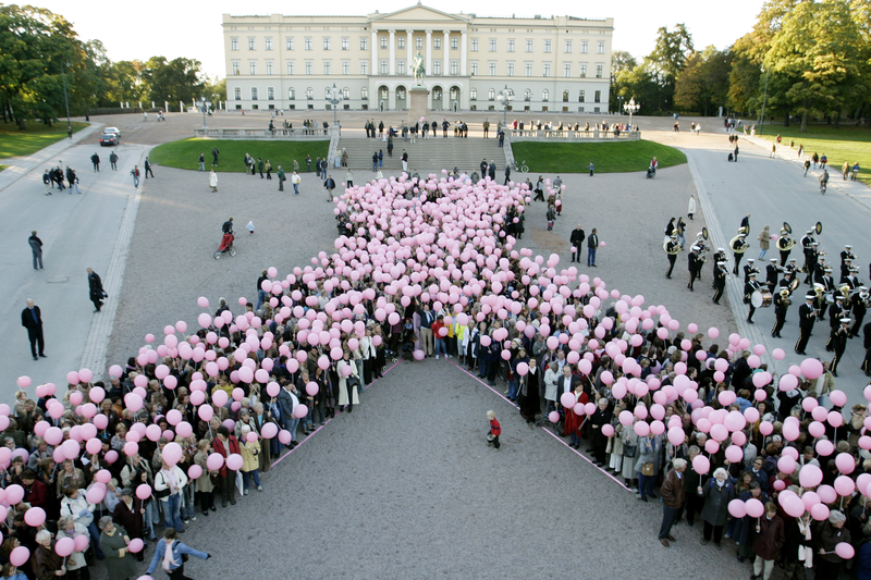 En stor gruppe mennesker danner et rosa bånd foran en bygning.