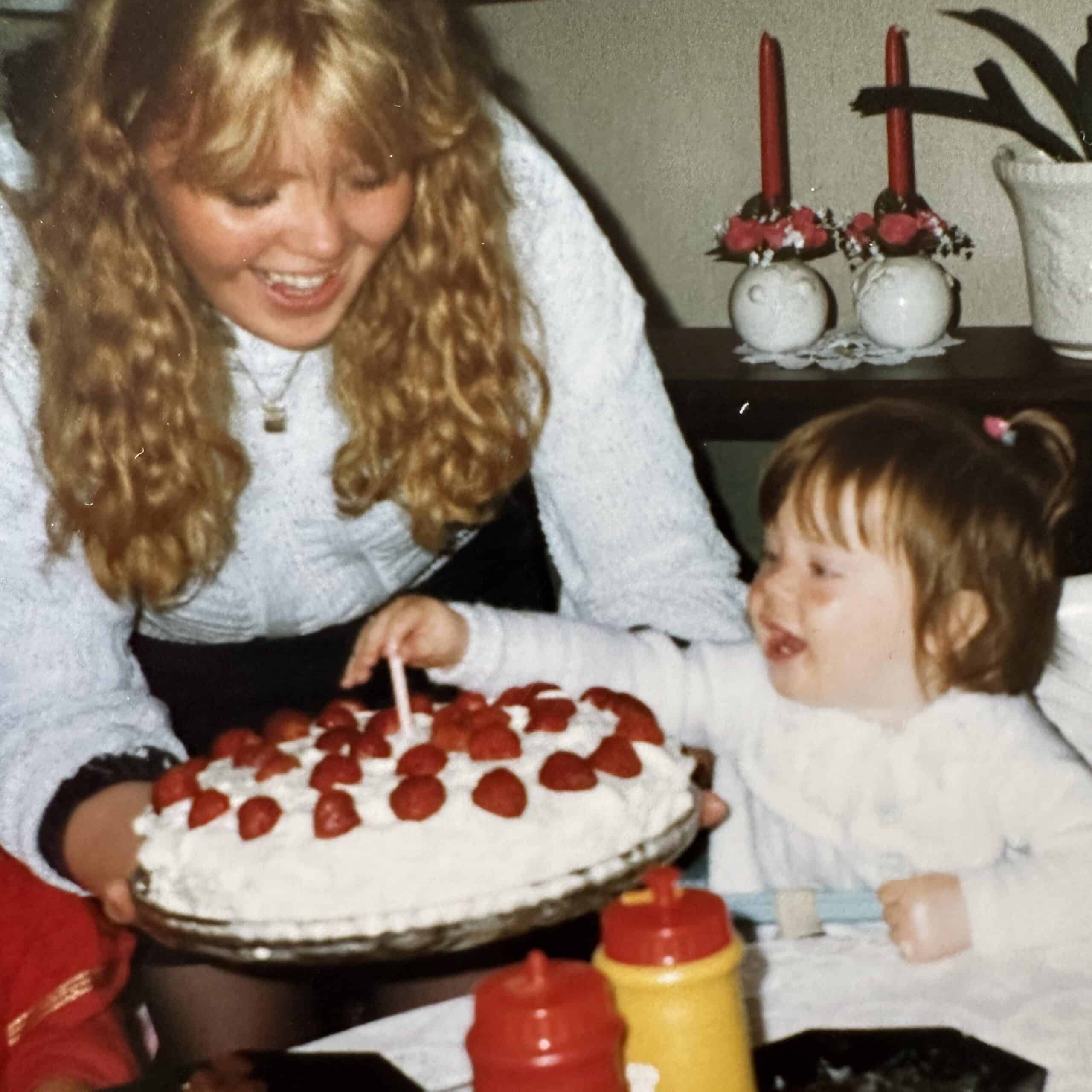 En kvinne med blondt hår blåser ut et stearinlys på en kake.