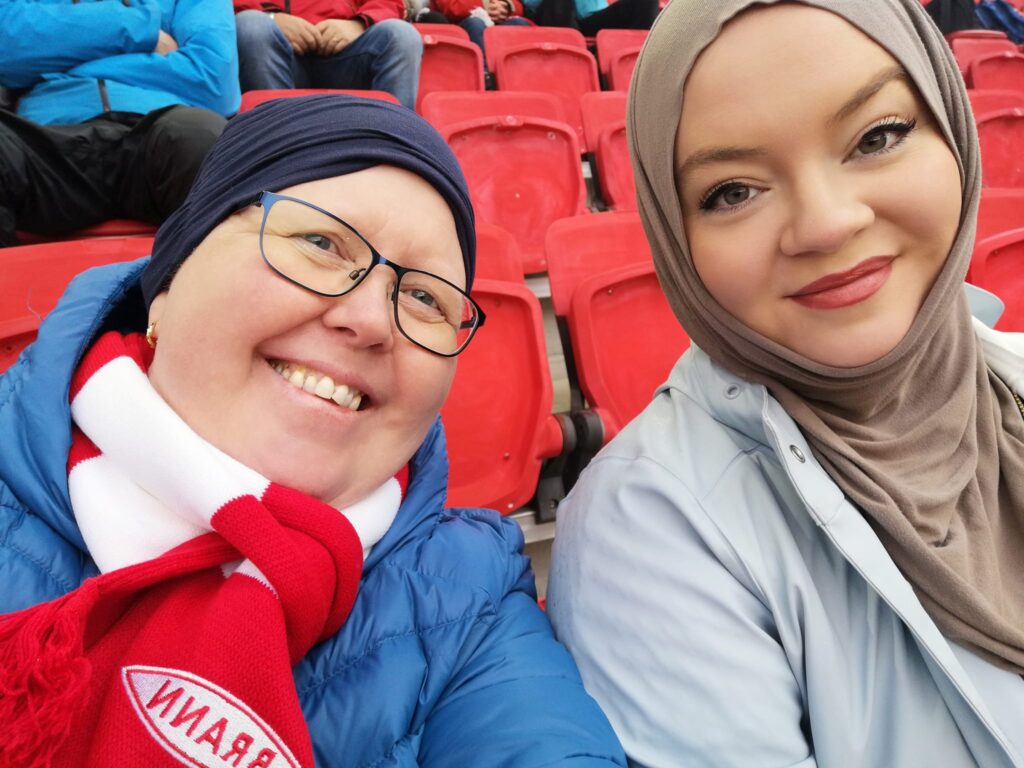 To kvinner sitter på tribunen på en fotballkamp.