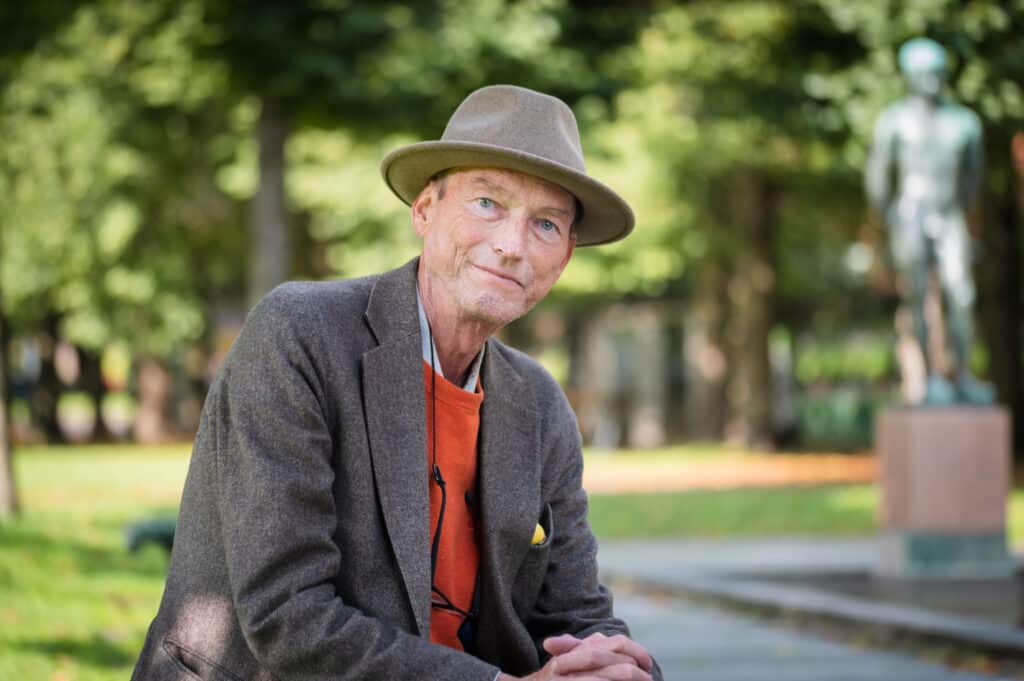 En mann i hatt sitter på en benk i en park.
