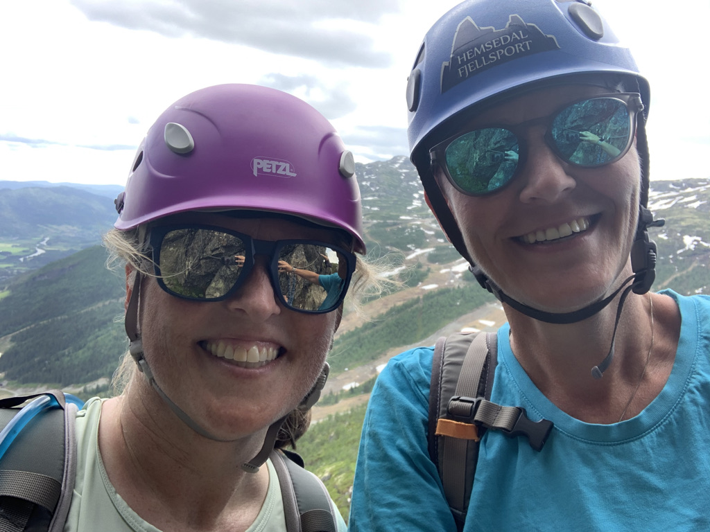 To kvinner med hjelmer og solbriller på toppen av et fjell.
