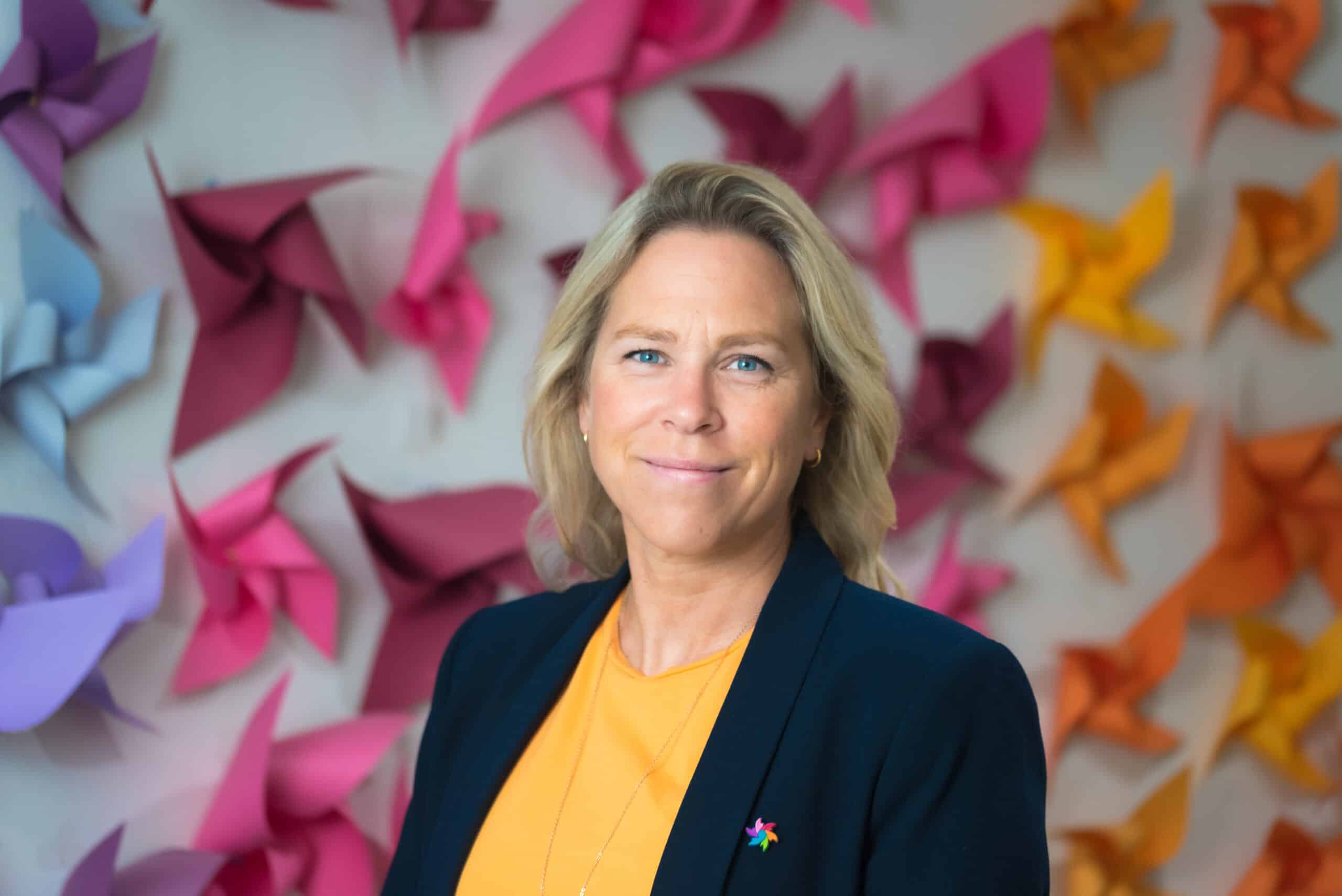 Anne Kari Prestegård som står foran en fargerik papirvegg og smiler.