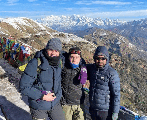 Tre menn poserer for et bilde på toppen av et fjell.