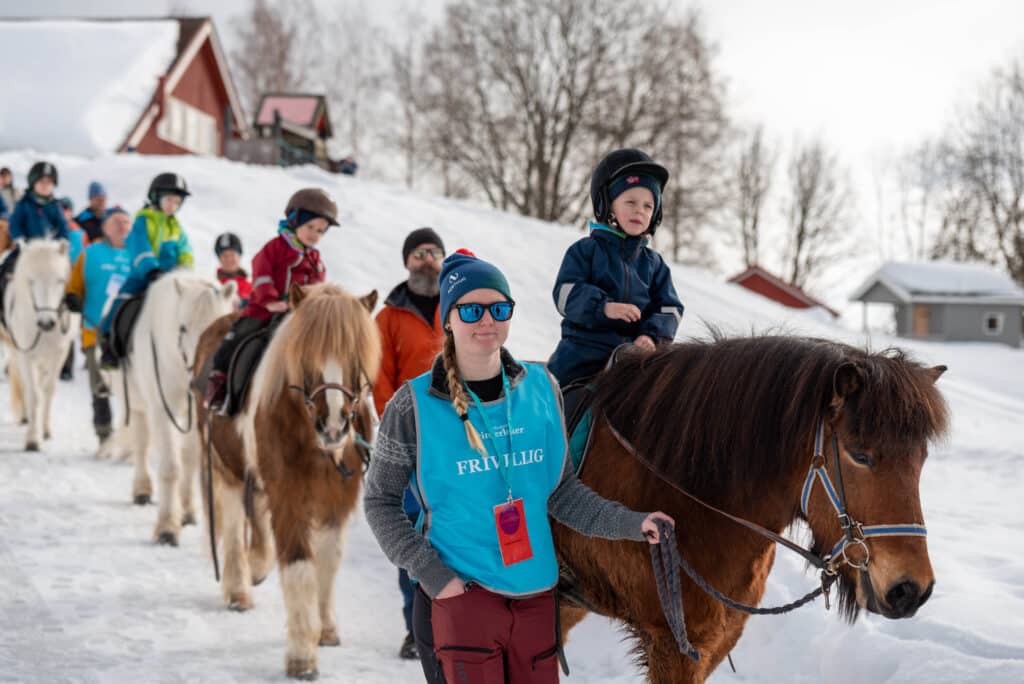 En gruppe mennesker som rir på hester i snøen.