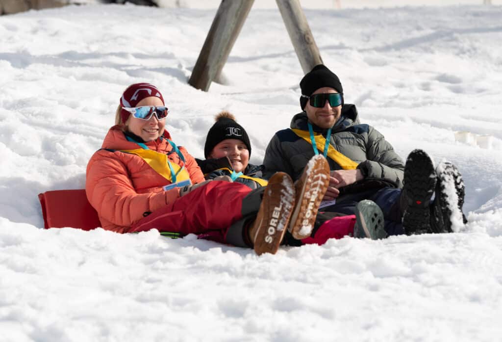 Tre personer sitter i snøen på en slede.