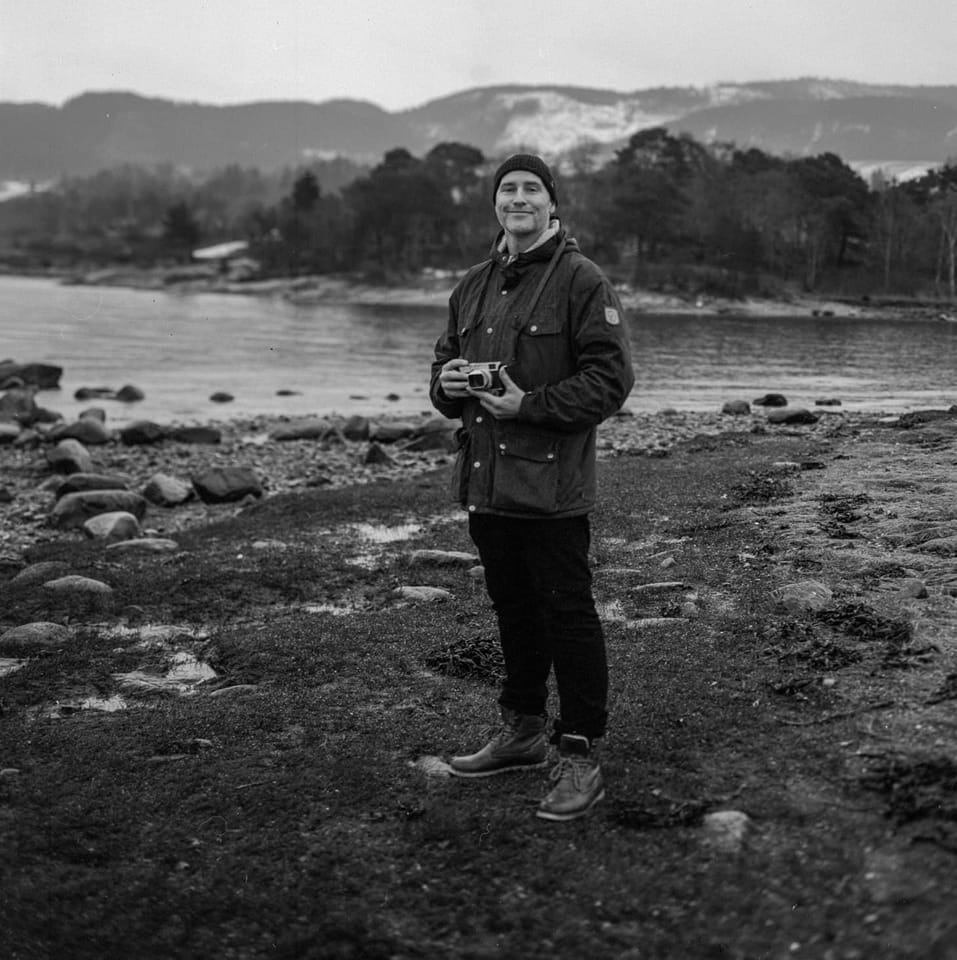 En mann som står på en steinete kyst med et kamera.