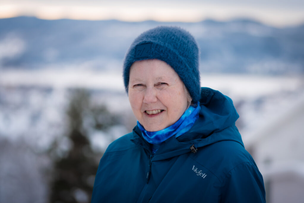Kvinne med blå lue og jakke står ute i snøen og smiler til kamera