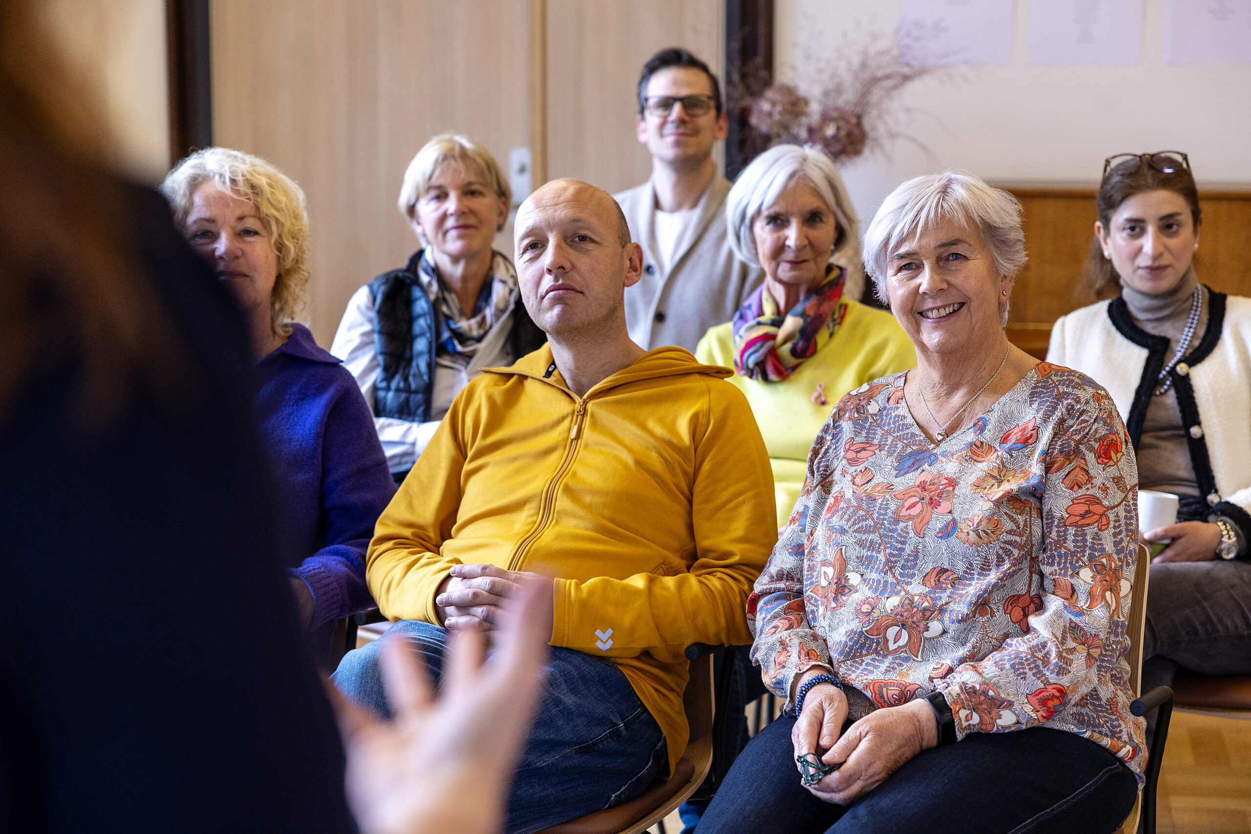 En gruppe oppmerksomme voksne som sitter og lytter til en usett foredragsholder under et møte eller seminar.