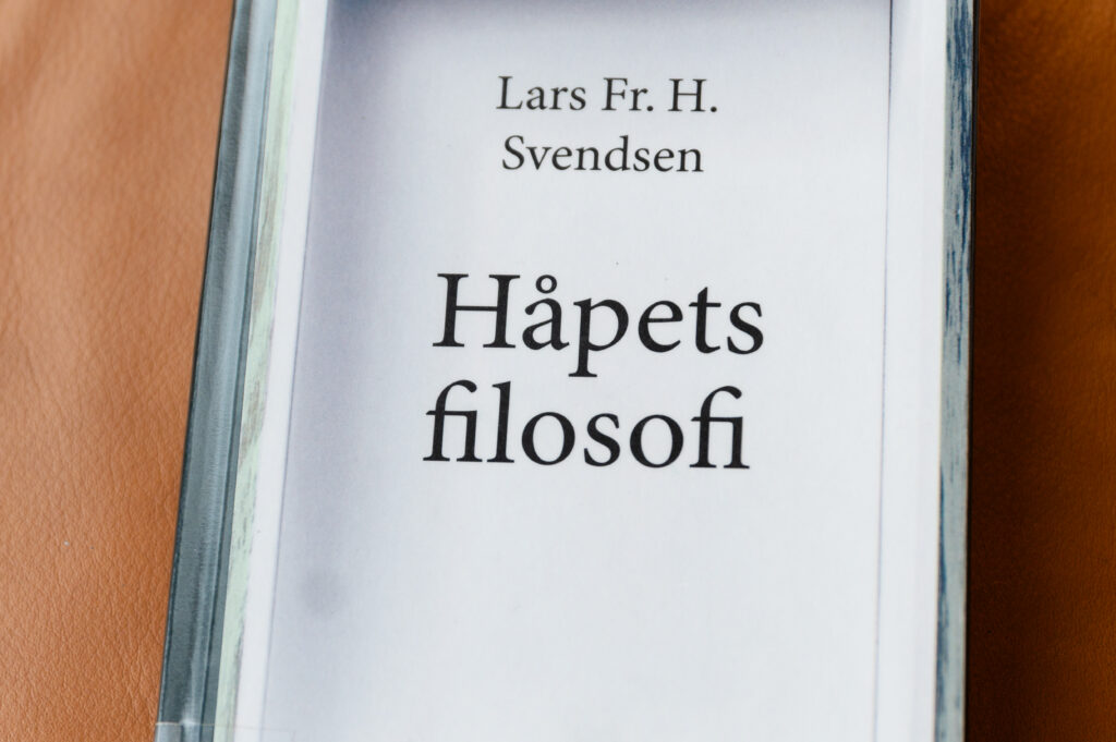 Nærbilde av et bokomslag med tittelen Håpets filosofi av Lars Fr. H. Svendsen, plassert på skinnoverflate.