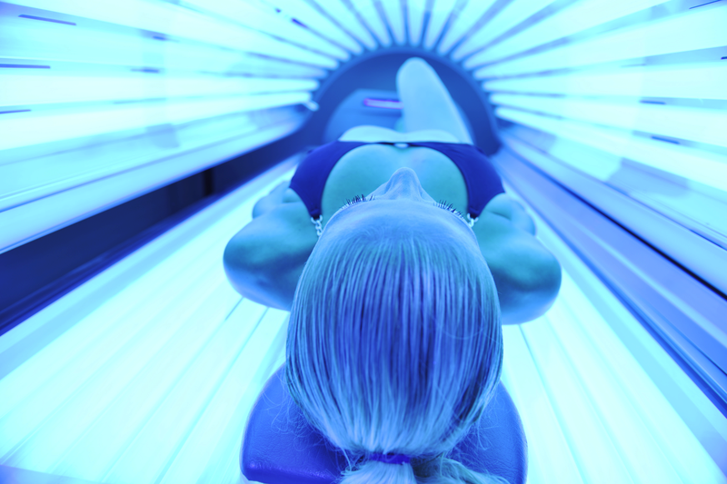 Person med blondt hår og svart badedrakt liggende i et opplyst solarium, sett fra nakkestøtten.