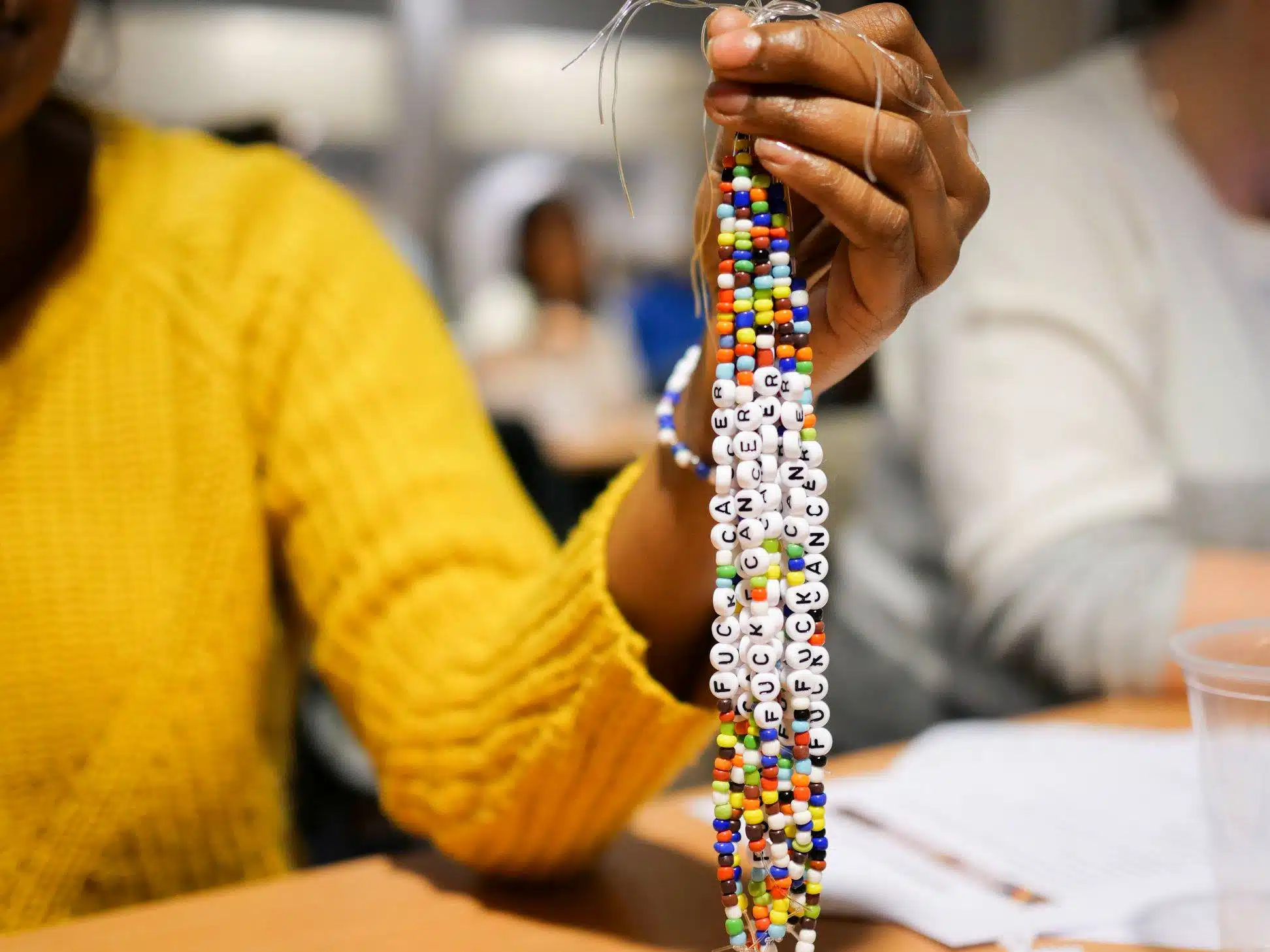 En person holder frem flere perlearmbånd med fargerike perler og hvite bokstavperler som staver FUCK CANCER.