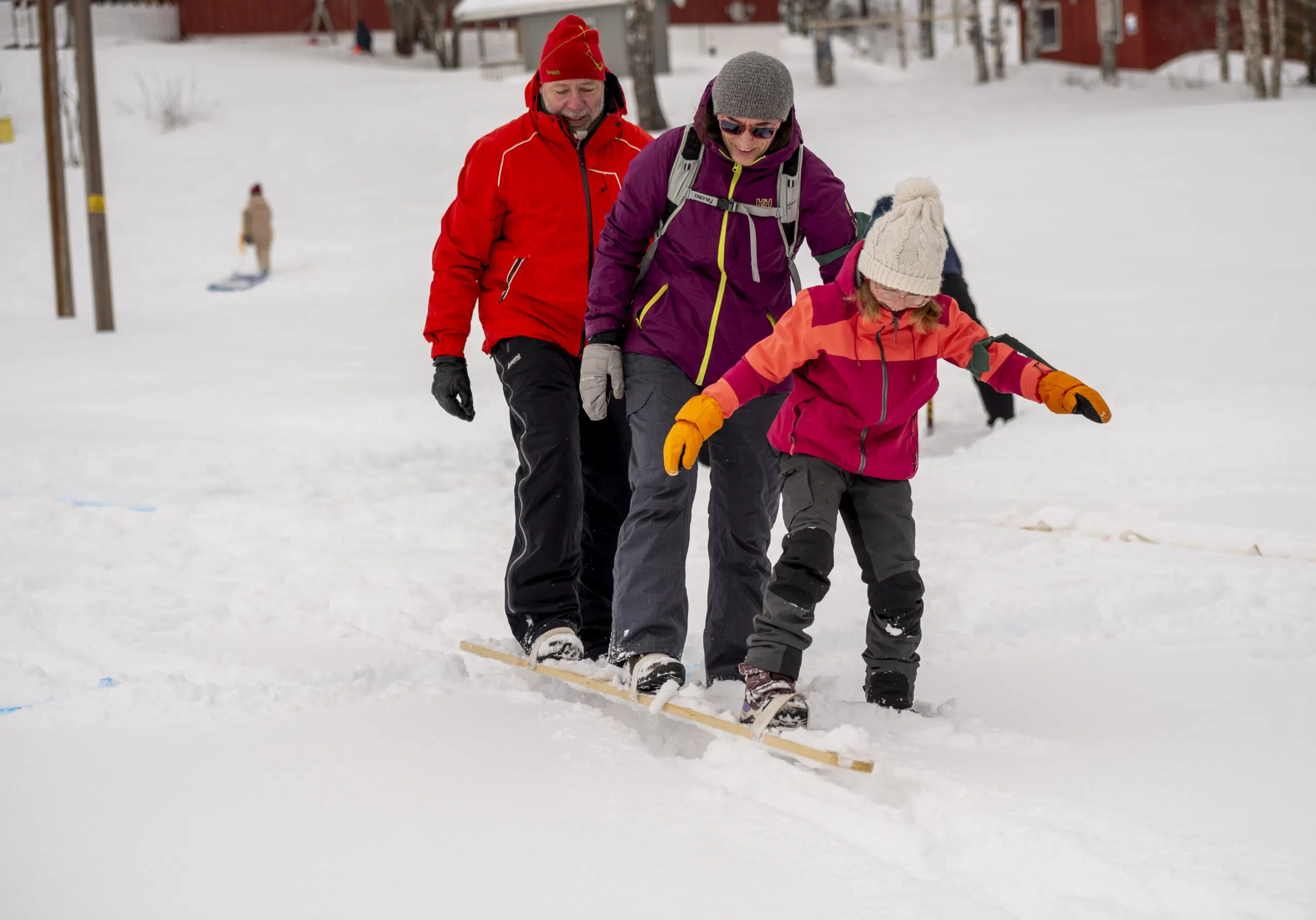 Tre personer i vinterklær går sammen på treski i et snødekt område, med en person som leder.