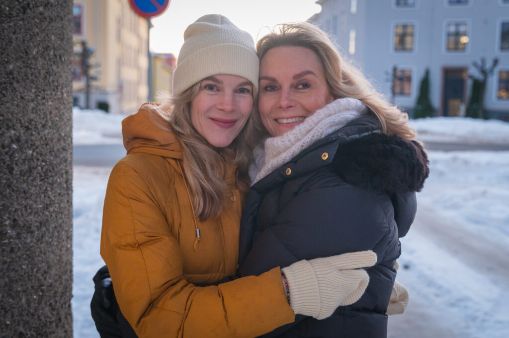 To kvinner holder rundt hverandre i en snødekt gate.