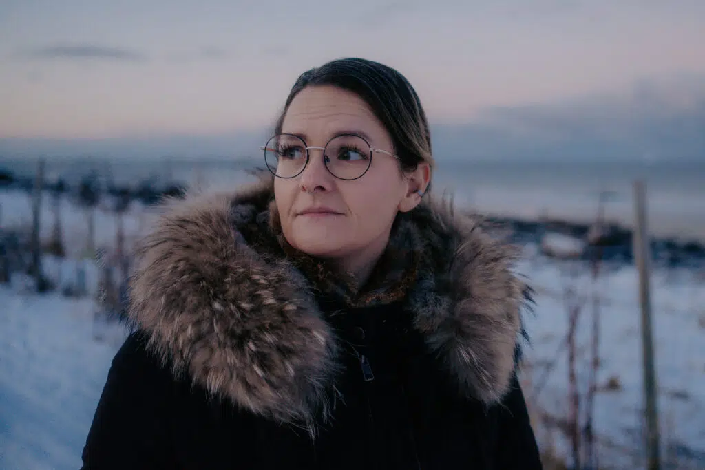 En person med briller og vinterfrakk med pelsfôret hette står utendørs i et snødekt landskap i skumringen og reflekterer over øyeblikket de tenkte: «Jeg prøver å sjekke meg for HPV-viruset.».