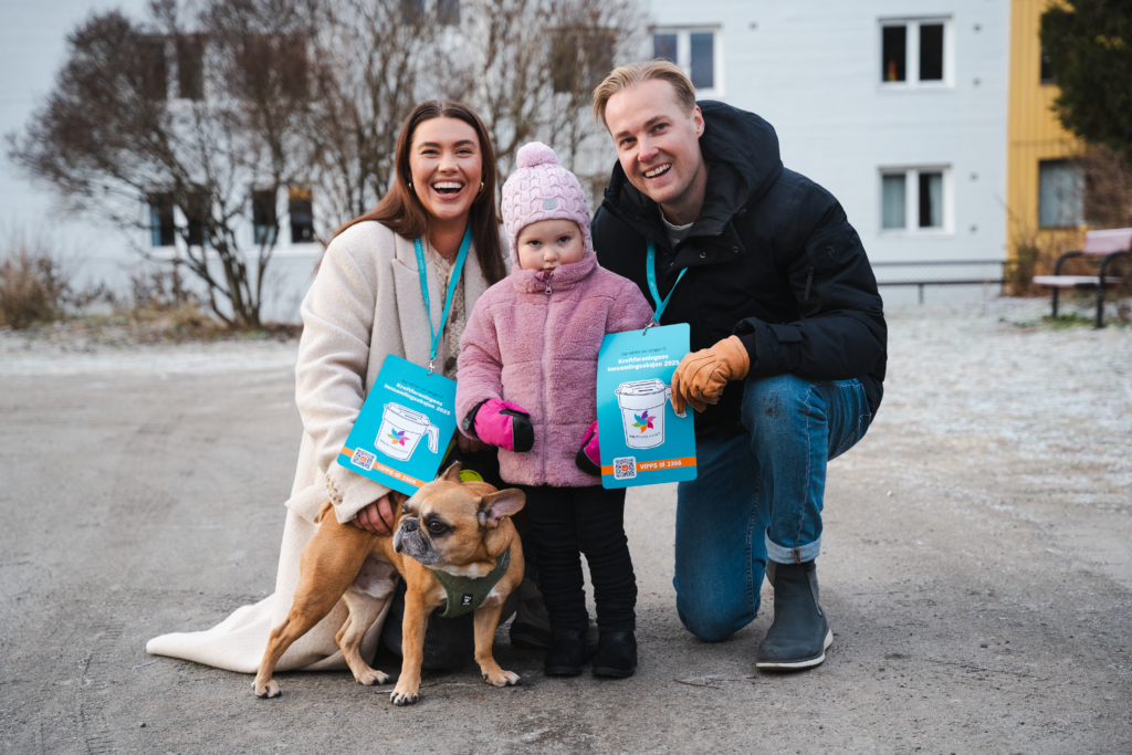 En kvinne, et barn og en mann står på en gårdsplass og smiler til kamera. Ved siden av kvinnen er det en hund. 