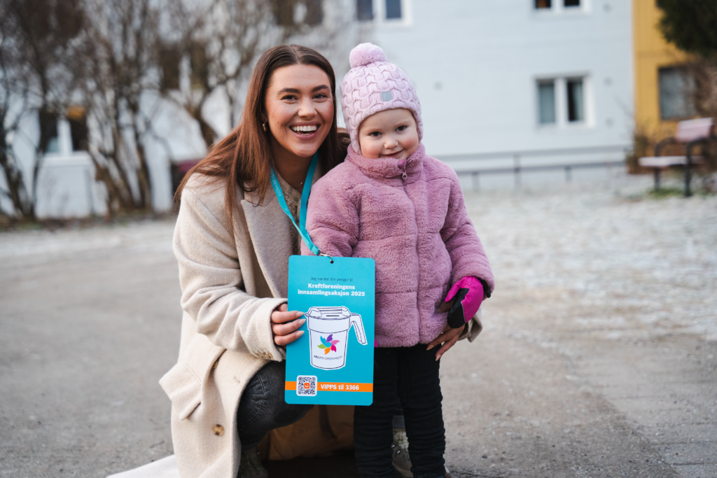 En kinne og et barn er ute på en gårdsplass og ser inn i kamera og smiler. 