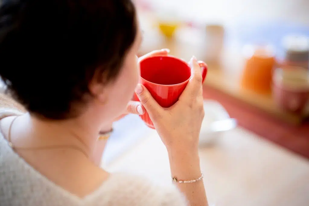 Person som holder et rødt krus med begge hender, sitter ved et bord.
