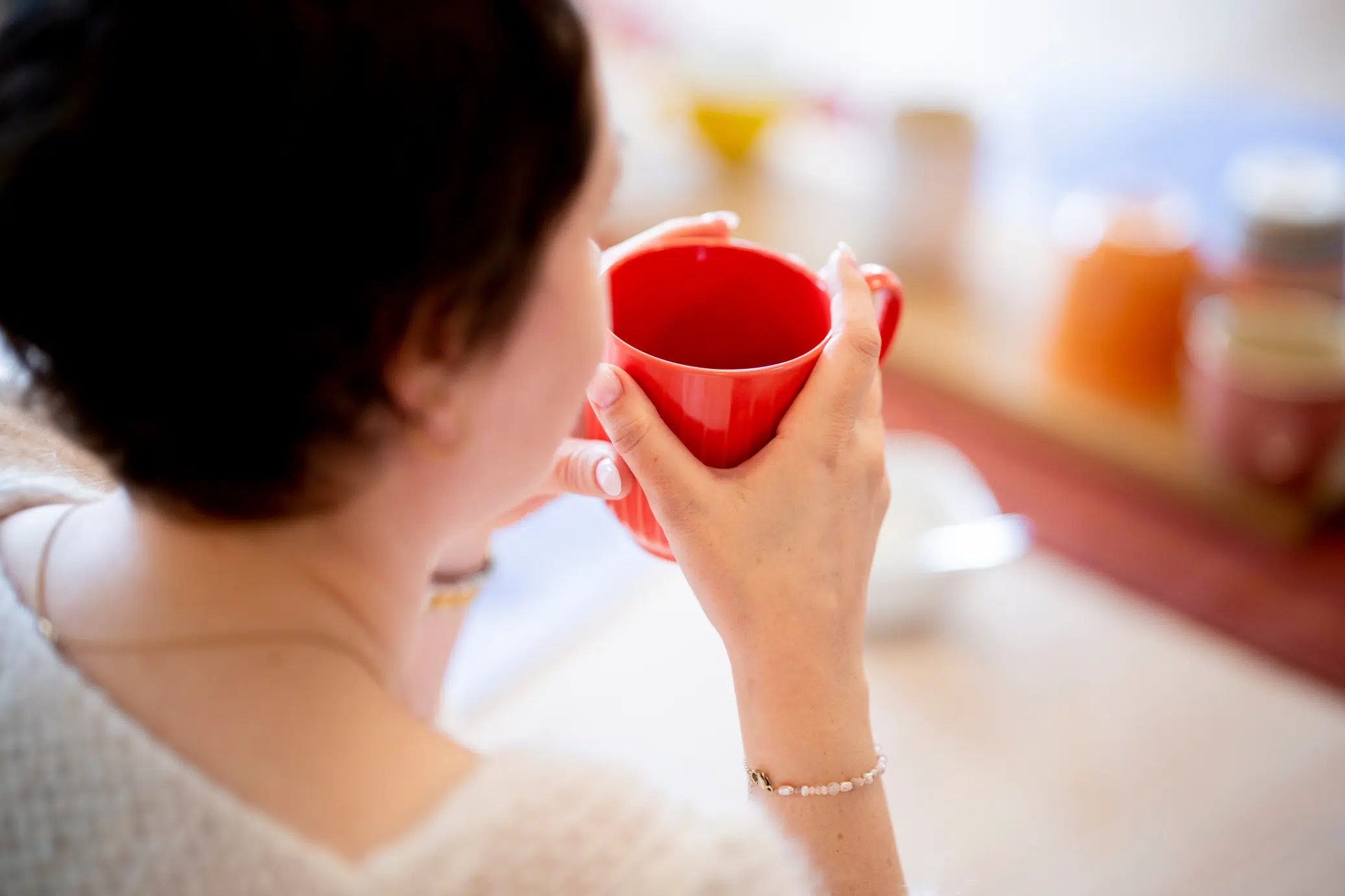Person som holder et rødt krus med begge hender, sitter ved et bord.