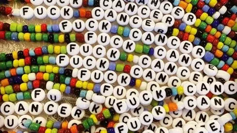 Perlearmbånd med hvite bokstavperler som staver "FUCK CANCER" ispedd fargerike perler.