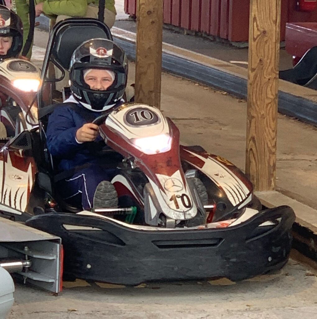 To personer med hjelm sitter i gokart under et treskur. Gokarten i forgrunnen har tallet 10 på seg.