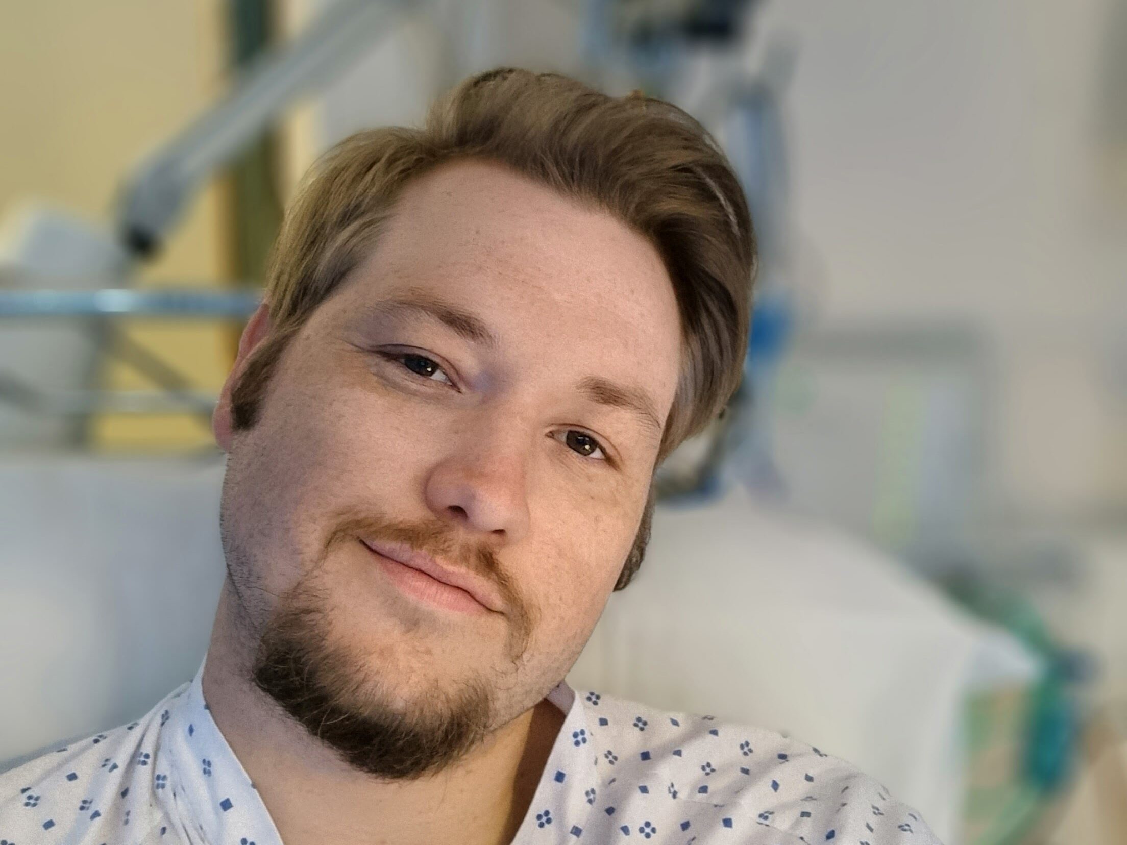 Person i sykehuskjole tar en selfie med medisinsk utstyr i bakgrunnen.