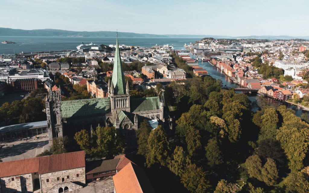 Luftfoto av en stor katedral omgitt av trær og bybygninger, med en elv og kystlinje synlig i bakgrunnen.