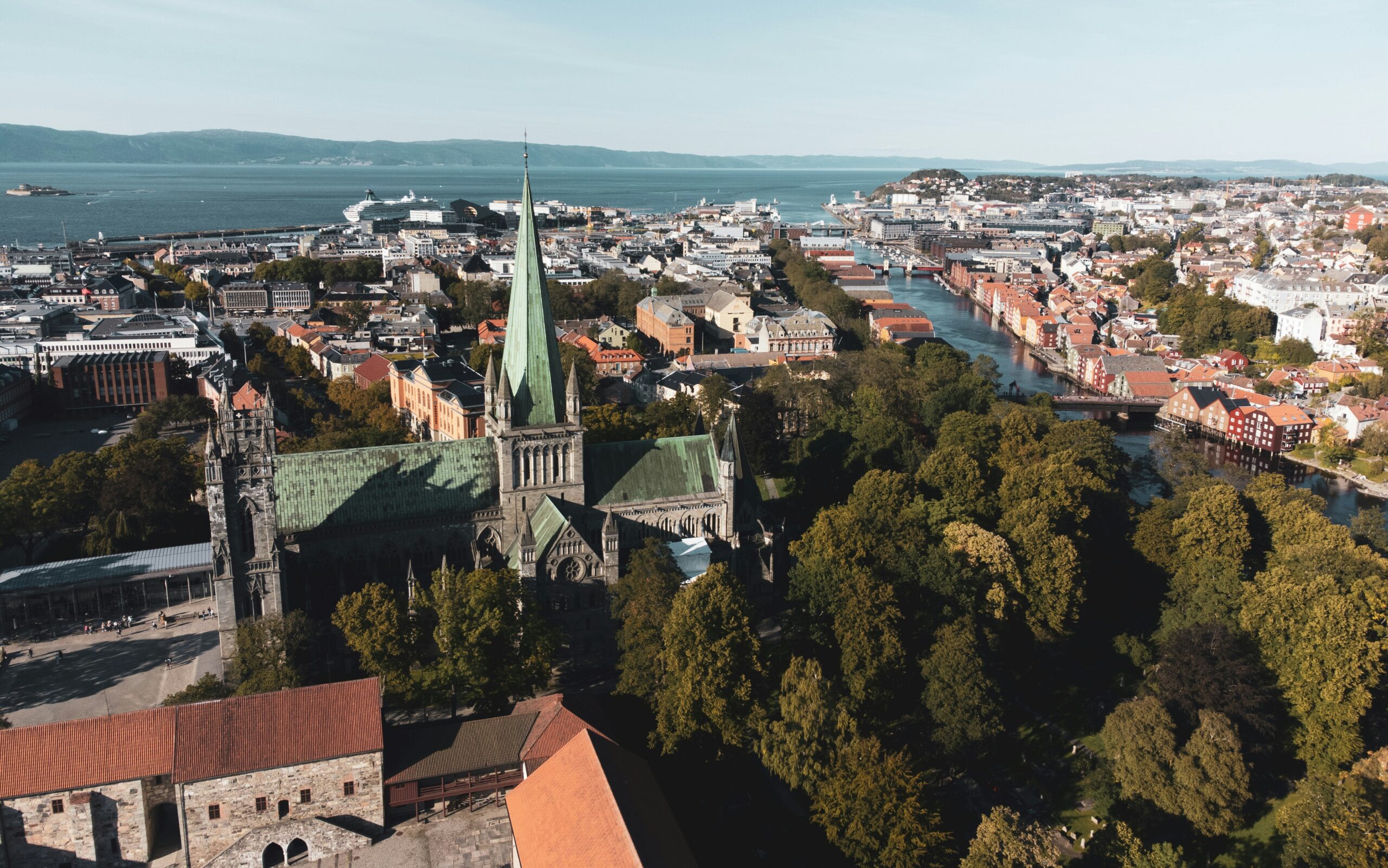 Luftfoto av en stor katedral omgitt av trær og bybygninger, med en elv og kystlinje synlig i bakgrunnen.